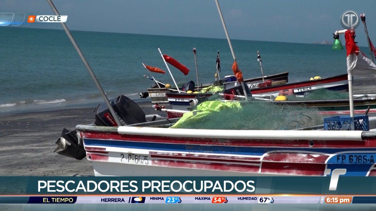 Coclé fishermen standing by small fishing boats at shore with fuel drums and nets, looking concerned about rising costs