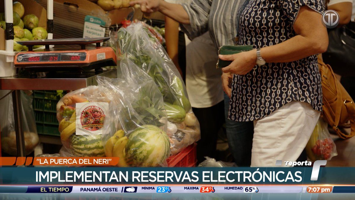 Market stalls at La Puerca del Neri fair with bags of fruits and vegetables and shoppers beneath municipal signage