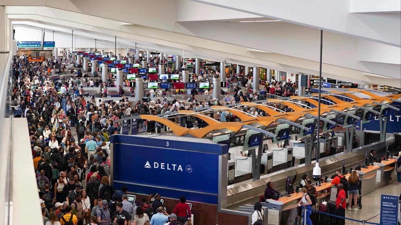 Passengers in line at a busy airport security checkpoint with TSA agents and X-ray screening machines