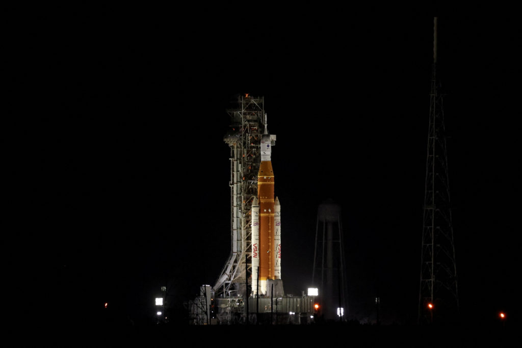 NASA officials speaking at a pre-launch briefing in front of a Space Launch System rocket graphic