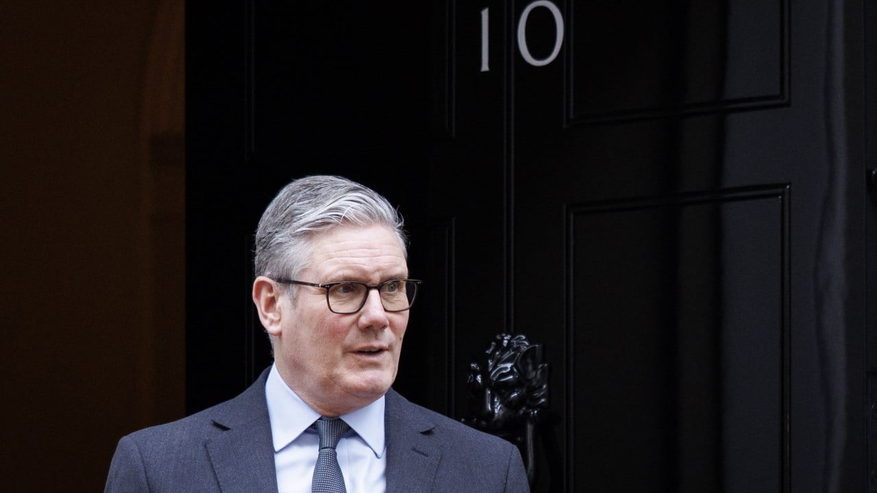British Prime Minister Keir Starmer speaking at a podium with government ministers and financial imagery representing markets
