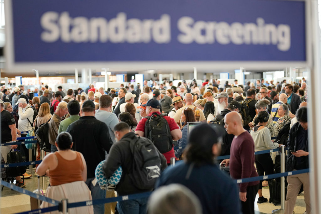 Long security lines at an airport checkpoint with travelers and TSA officers managing the queue