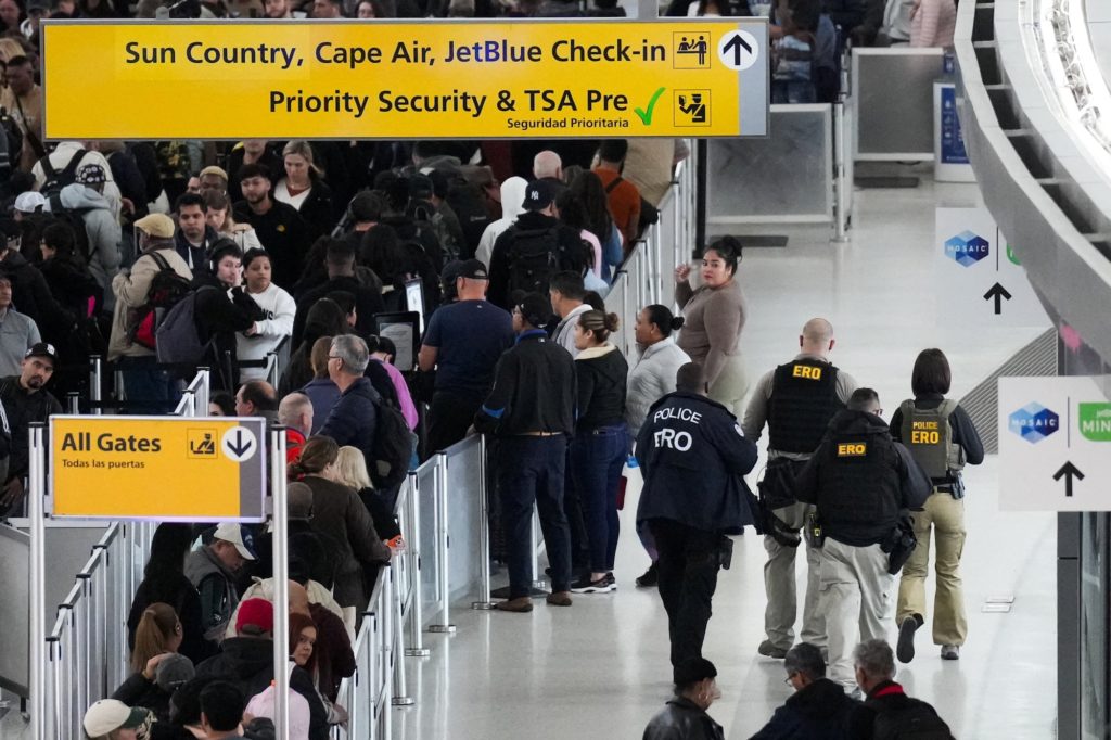 ICE officers near an airport security checkpoint assisting with operations at a busy terminal