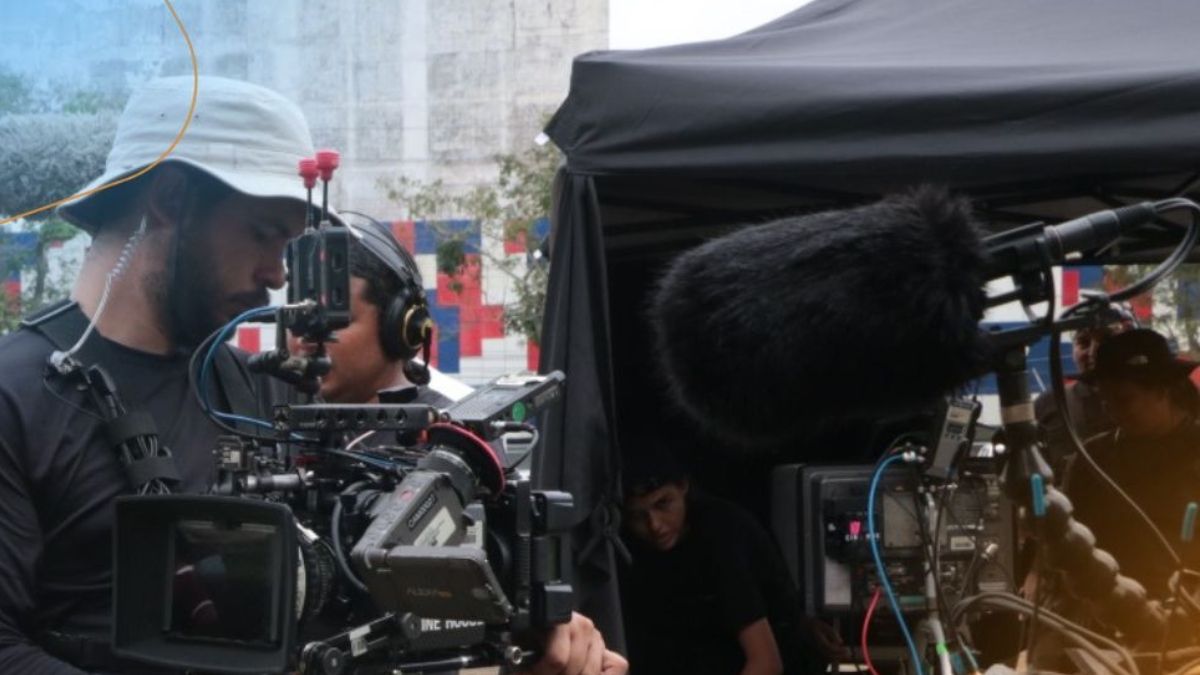 A filmmaker operating a camera with a clapperboard and a Panamanian flag in the background, representing a scholarship to study film in India