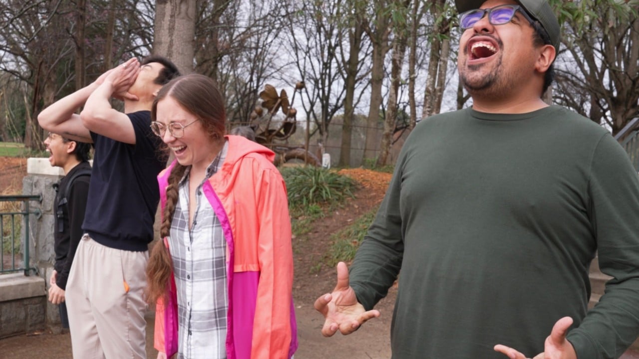 A small group of people outdoors near water in Seattle raising their heads and shouting together during a scream club session