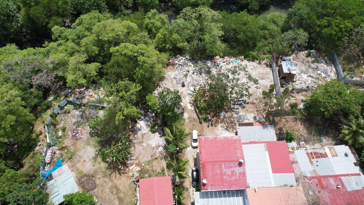 Illegal waste dump near wetlands and residential homes in Panamá Viejo, showing contaminated shoreline and nearby vegetation