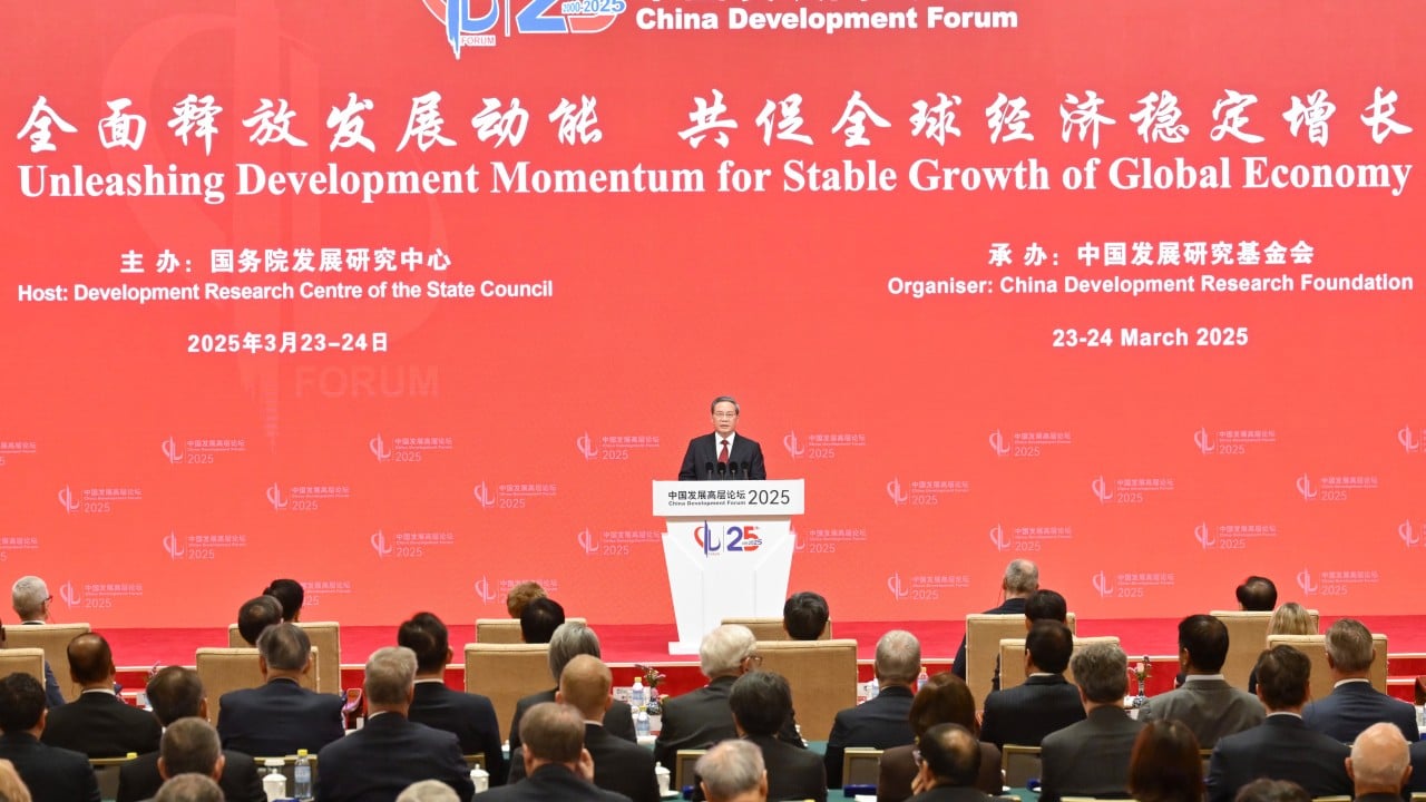 International business delegates seated in a conference hall at the China Development Forum in Beijing, with a stage and presentation screens visible