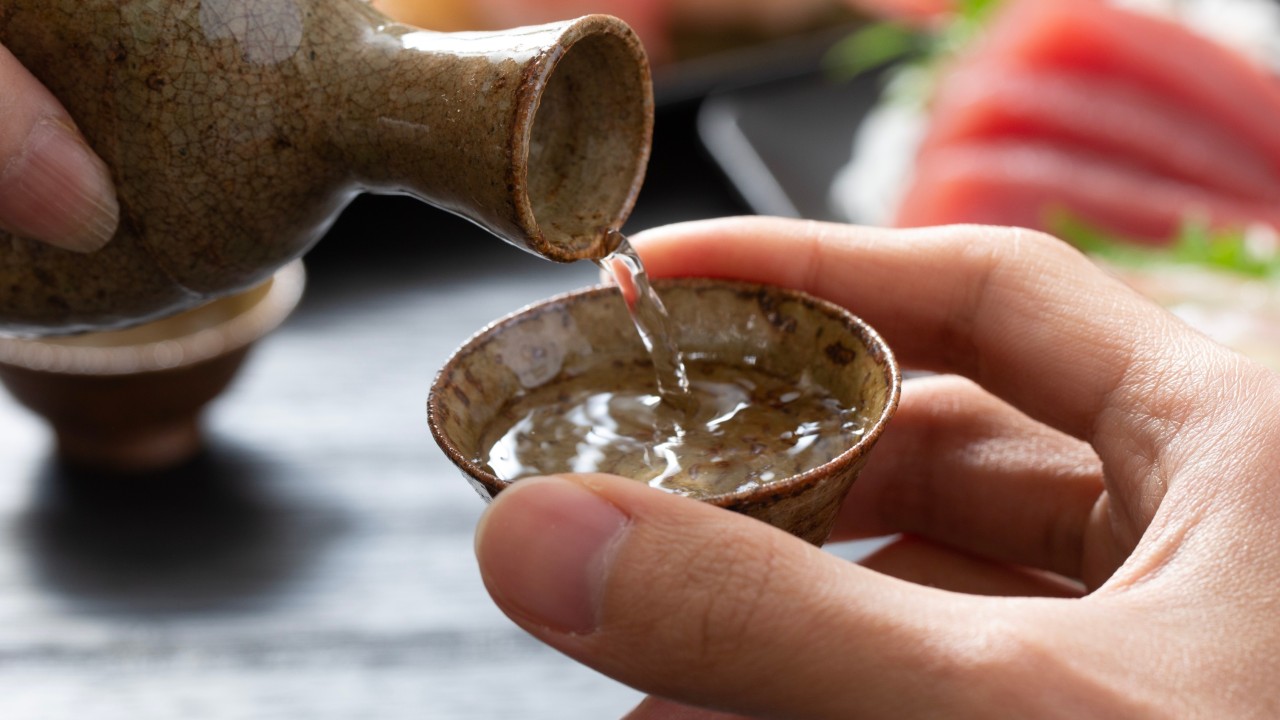 Bottles and cups of sake beside rice grains and a small dish, illustrating a traditional Japanese rice-based beverage