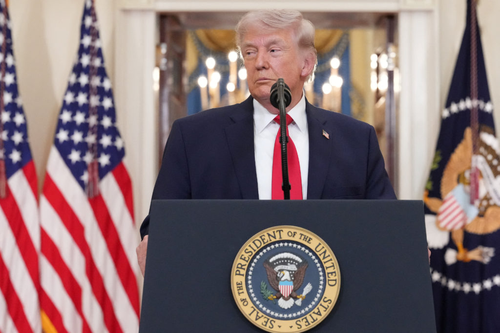 President Donald Trump speaking about the Iran conflict at a podium with the U.S. flag behind him