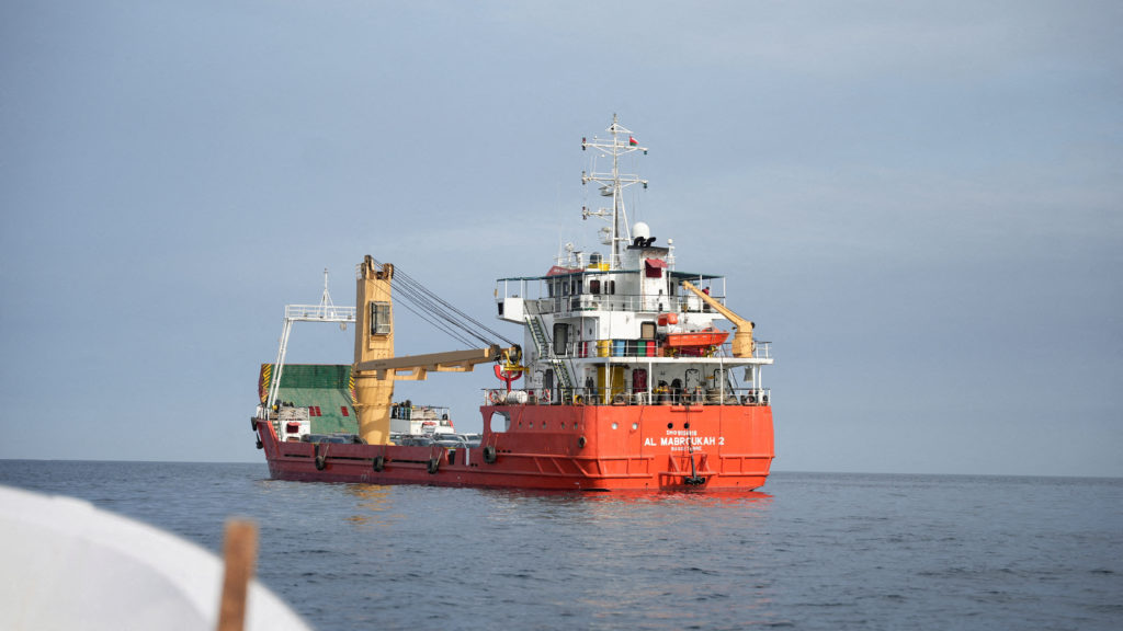 Oil tankers navigating a narrow maritime chokepoint with naval vessels in the distance