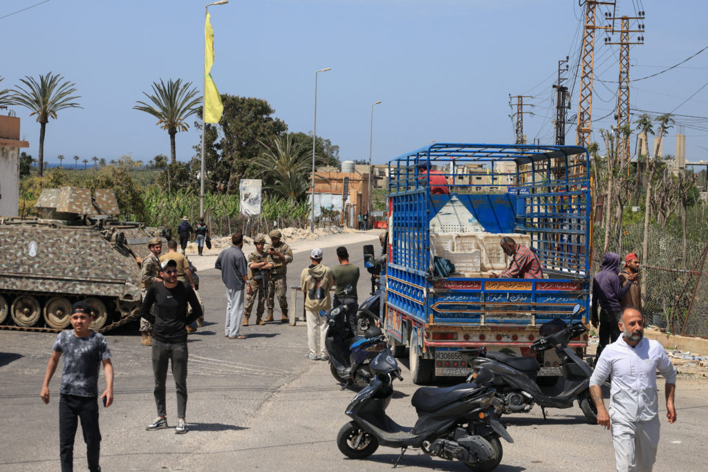 Israeli and Lebanese flags shown side by side with a tense border landscape in the background
