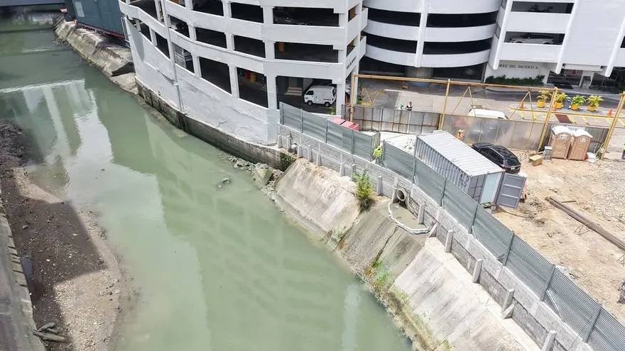 Construction site near an urban river in Panama City with muddy water and environmental officials nearby