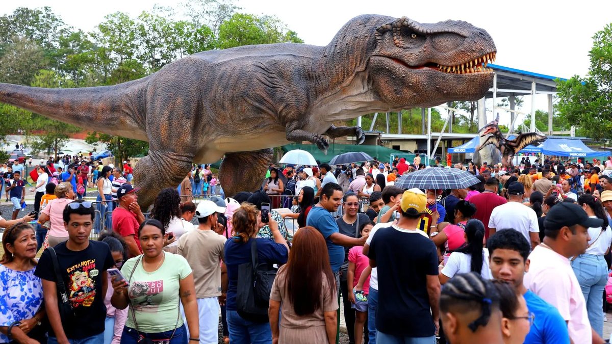 Families attending a dinosaur-themed outdoor event at Parque Norte with shuttle buses nearby
