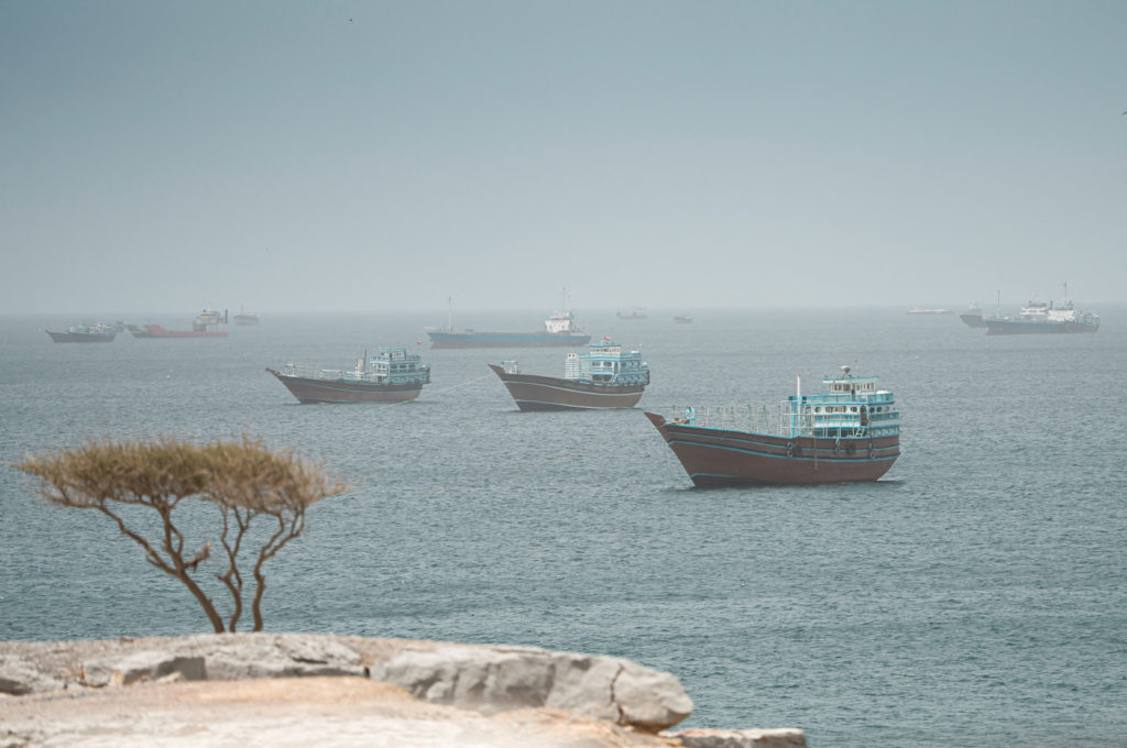 An Iranian-flagged oil tanker sailing at sea with naval vessels nearby in the Gulf of Oman.