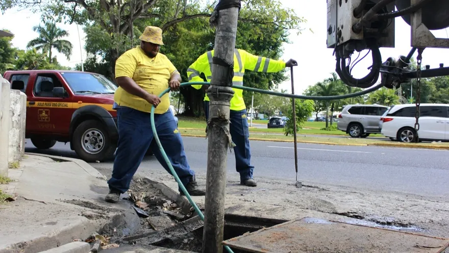 Workers cleaning drainage drains in a flooded-prone Panama City neighborhood near busy streets and low-lying buildings