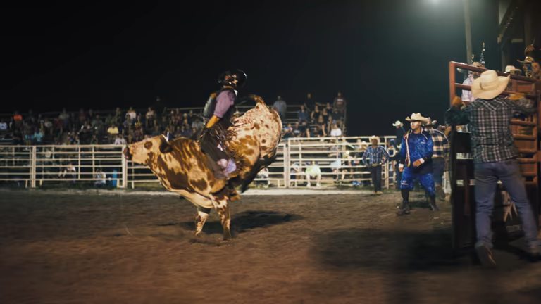 Cowboys on horseback performing at a rodeo arena with riders and spectators in a large stadium setting